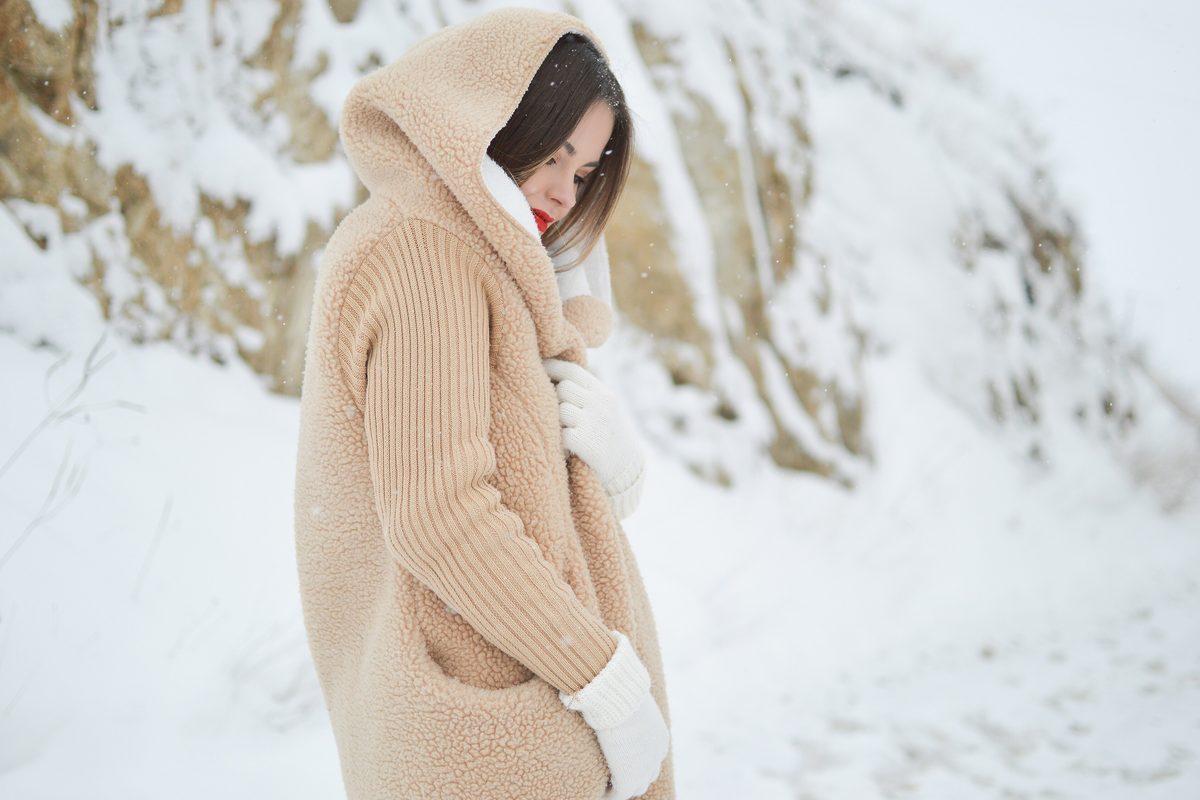 A woman in a camel hooded coat walks a snowy mountain path