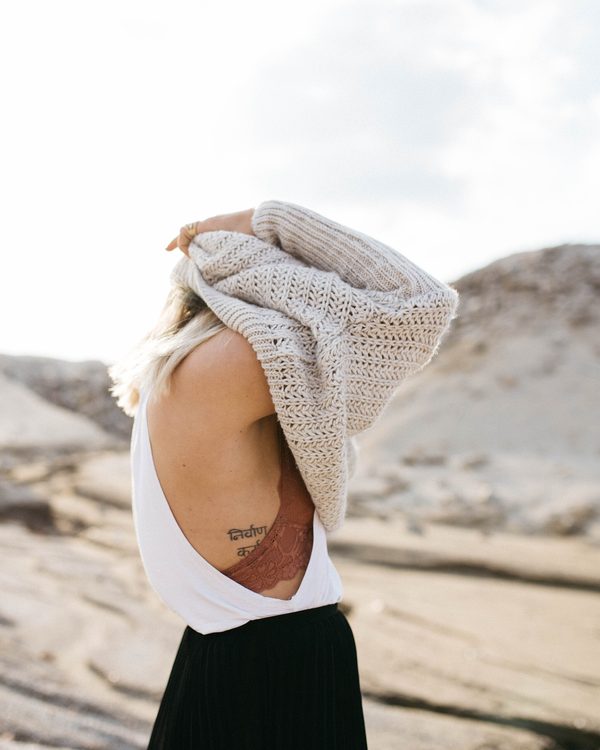 A woman pulls on an oatmeal chunky knit sweater among pale rocks