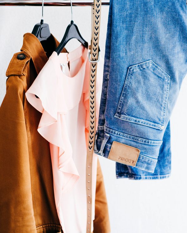 A camel jacket, a pink blouse and jeans hanging on a white rail