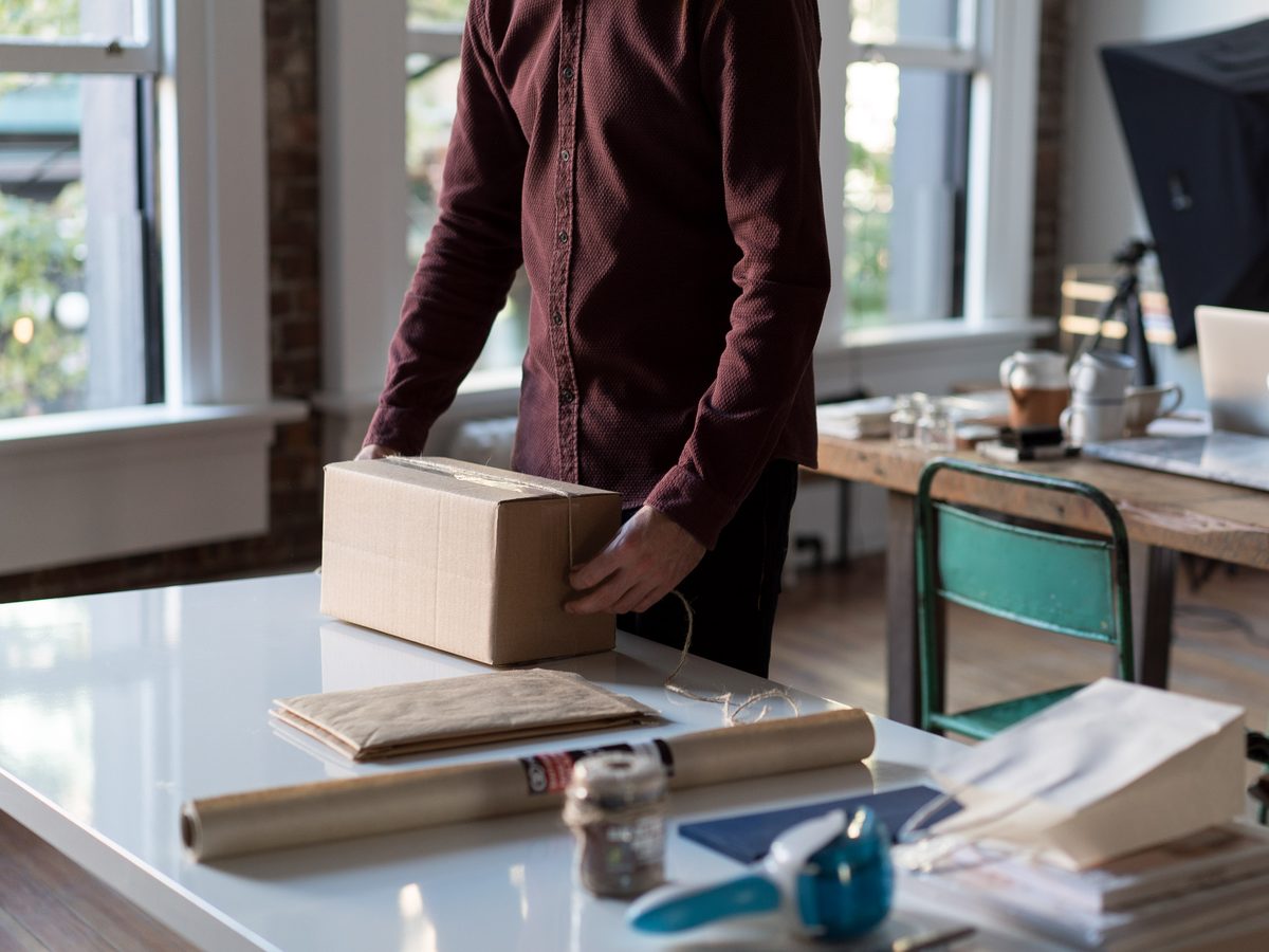 A person tapes a brown parcel shut on a white studio table