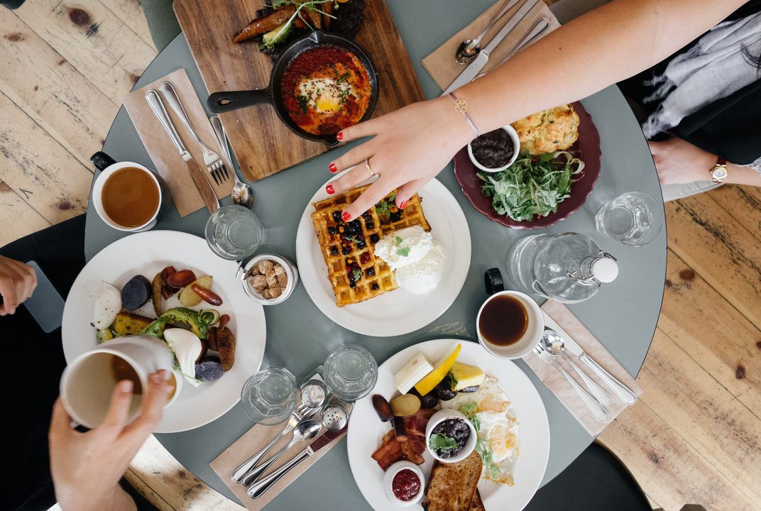 Friends sharing waffles, eggs and coffee at a round brunch table seen from above