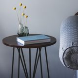 Round dark side table with books and a small vase of yellow flowers