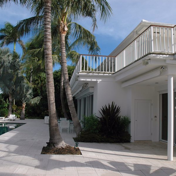 White villa with a spiral staircase beside a pool and palm trees