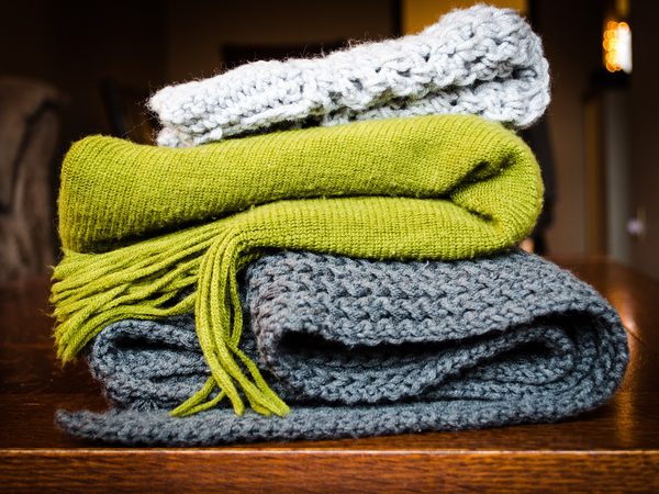 A stack of folded knitted blankets in green, grey and white