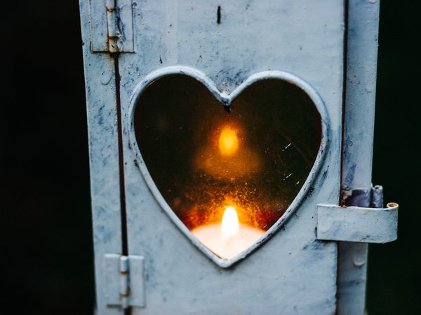 A candle glowing through a heart cut into an old metal door