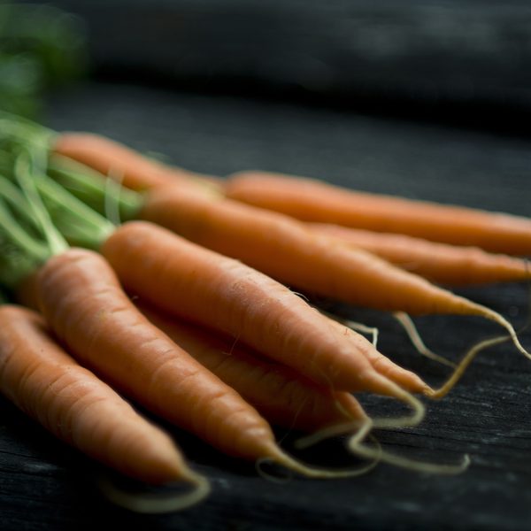 A bunch of carrots with their green tops on a dark board