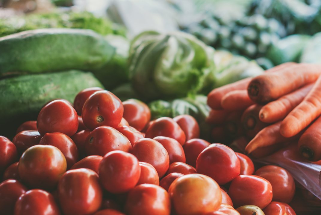 Market stall piled with red tomatoes, carrots and green squash