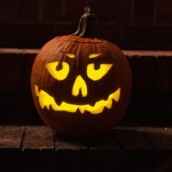 A carved pumpkin with a glowing grin on old brick steps