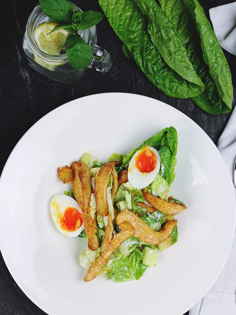 Romaine salad with crispy chicken strips and halved boiled eggs on a white plate