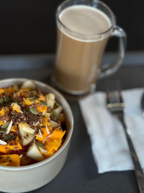 Bowl of roasted squash, apple and seeds next to a glass of milky coffee