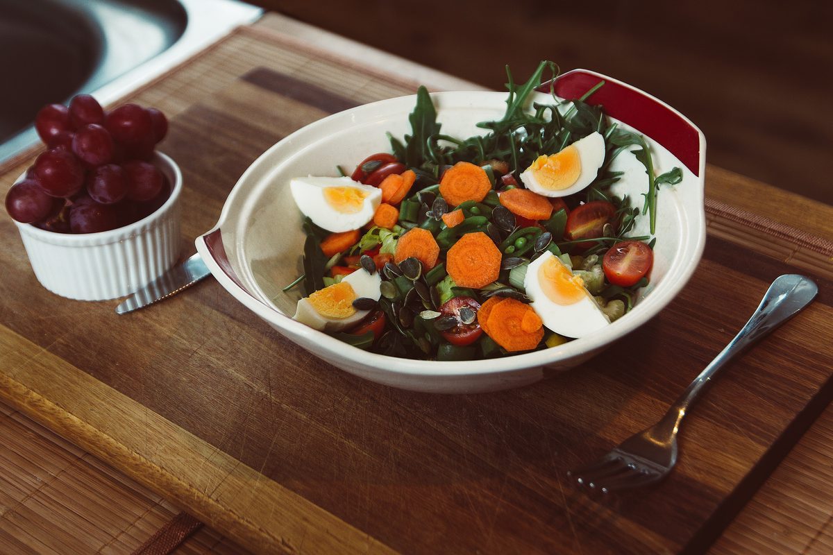 Salad of greens, carrots and boiled eggs in a white bowl on dark wood