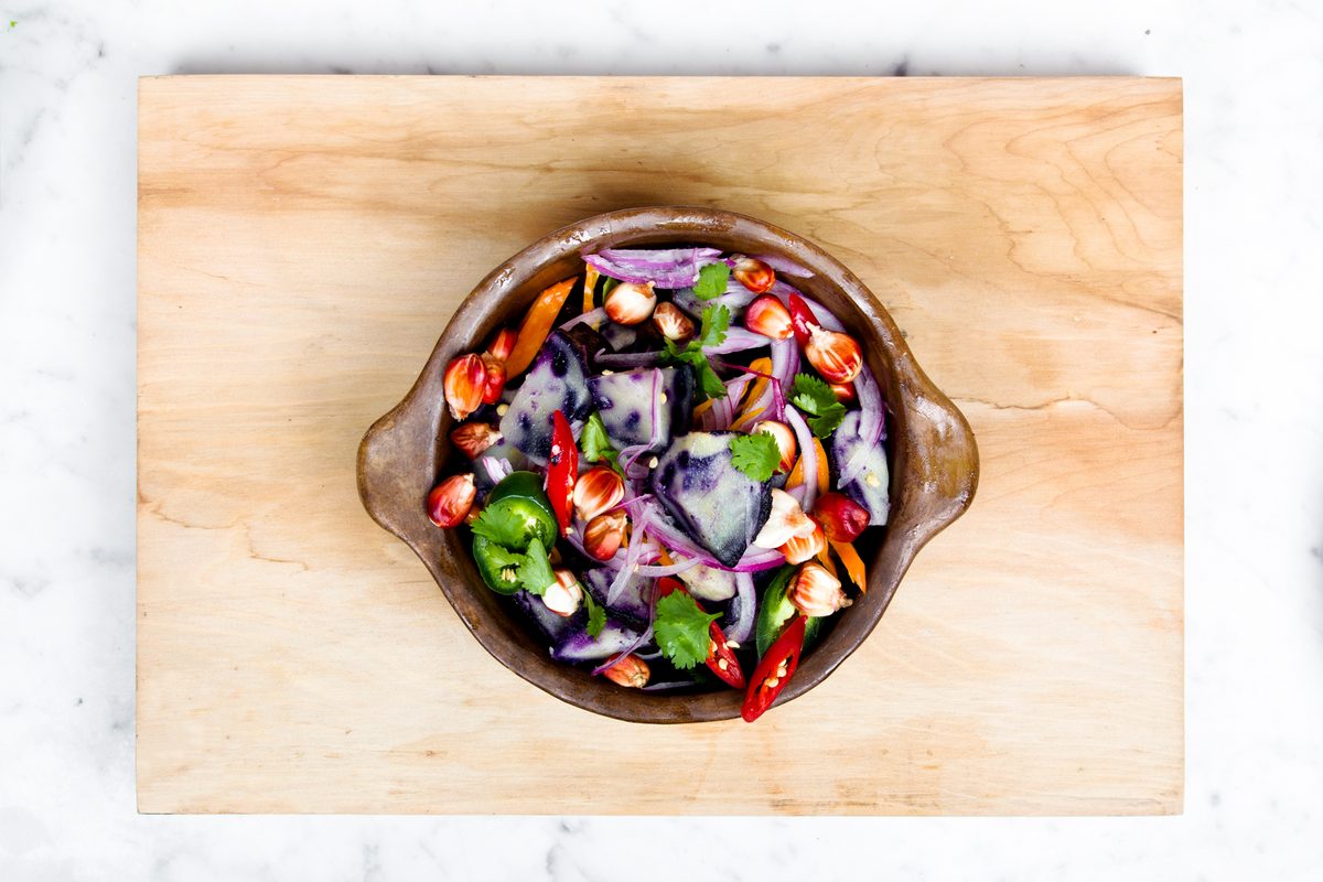A bowl of red cabbage, peppers and herbs on a wooden board seen from above