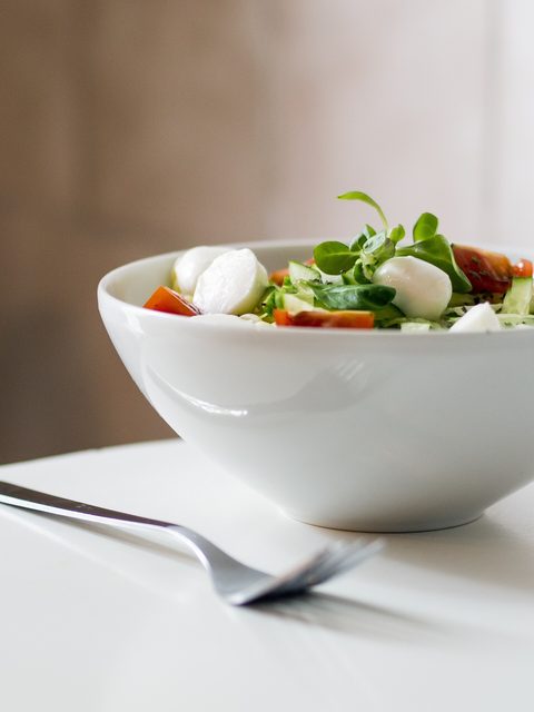A white bowl of leafy salad with mozzarella and tomato