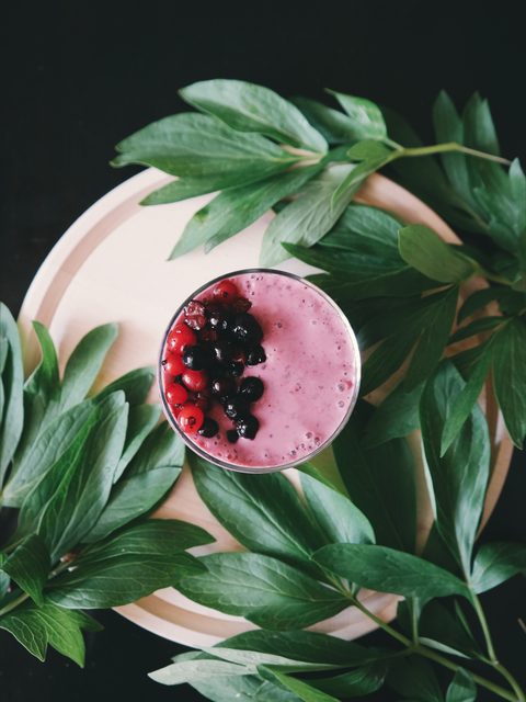 A pink berry smoothie bowl surrounded by green leaves
