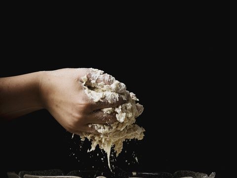 Hands lifting wet dough out of a metal bowl