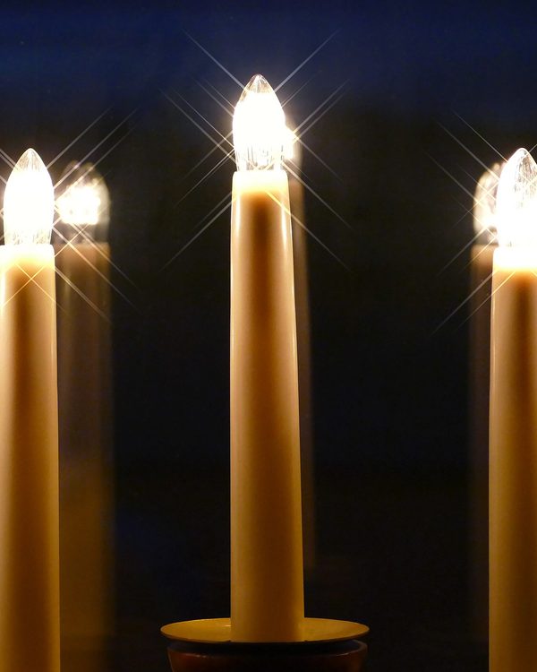 A row of tall candle lights glowing against a dark night