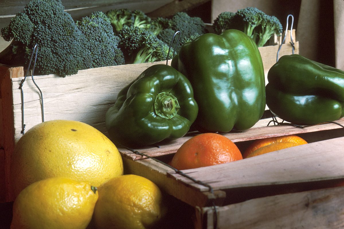 A wooden crate of broccoli, green peppers, grapefruit and oranges