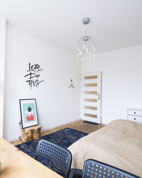 A bright bedroom with a floor lamp, a plant and a navy rug