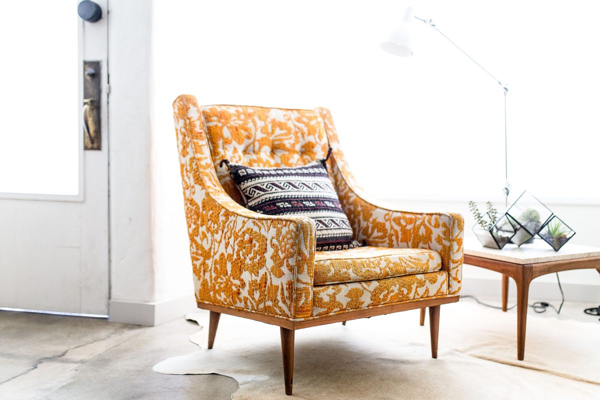 A mustard patterned armchair with a striped cushion beside a wooden coffee table