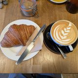 A croissant and a latte with leaf art on a wooden table
