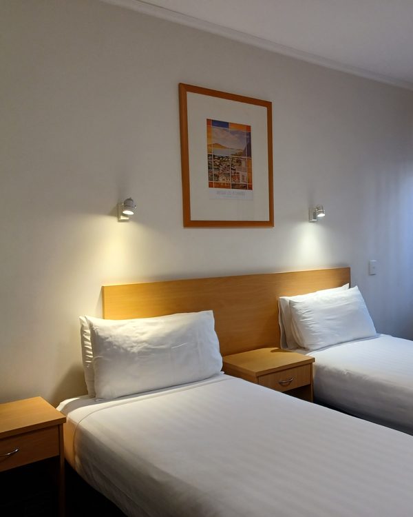 A calm hotel room with twin beds, wall lamps and a framed print