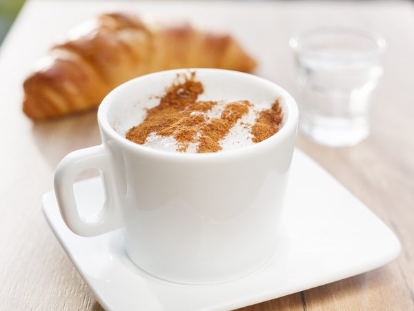 A cappuccino with cinnamon and a croissant on a light wooden table