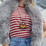 Gold pendant necklace worn over a striped top and grey fur