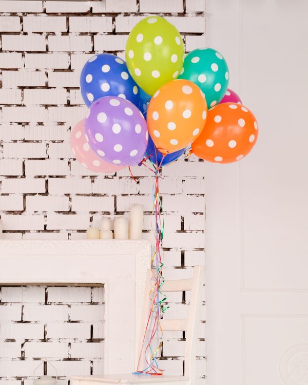Colorful polka dot balloons tied together against a white brick wall