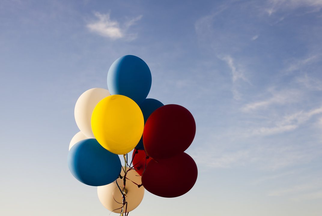 A bunch of yellow, blue and red balloons floating against a clear sky
