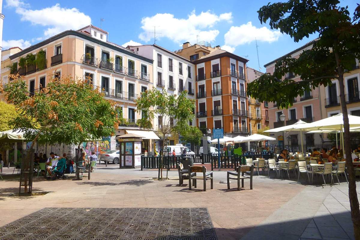 Sunny Madrid plaza with cafe umbrellas, trees and tall apartment buildings