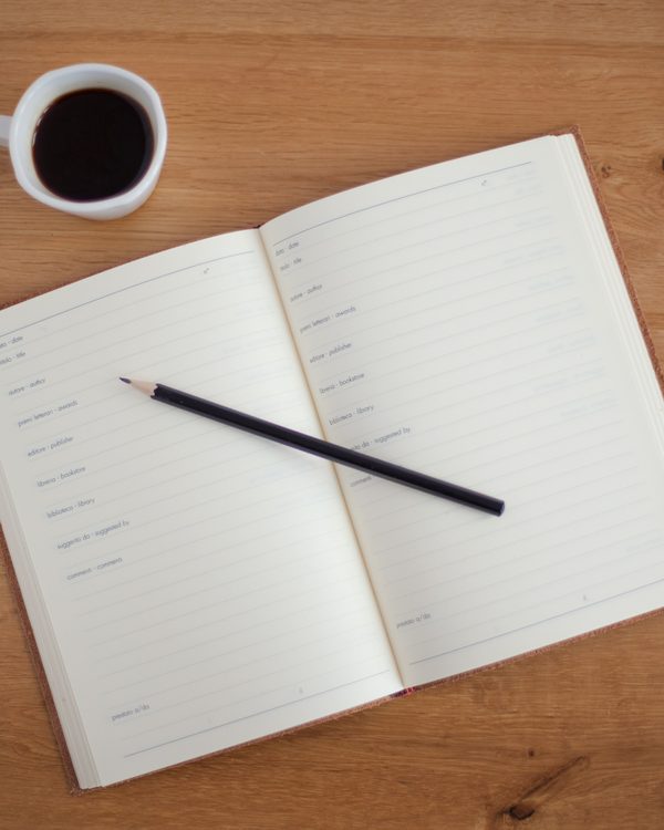 Open notebook with a pencil beside a cup of black coffee on a wooden table