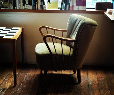 Green wingback armchair by a sunny window with a bookshelf above