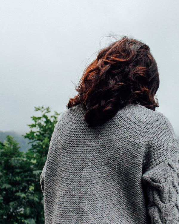 Woman in a grey cable knit jumper looking at green hills