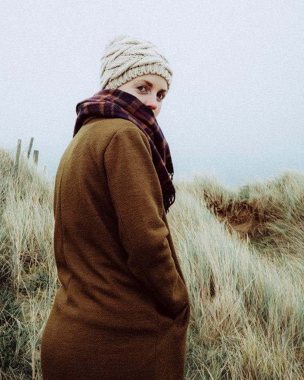 Woman in a long brown coat and knit hat in coastal grass