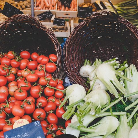Baskets of ripe tomatoes and fresh fennel on a market stall