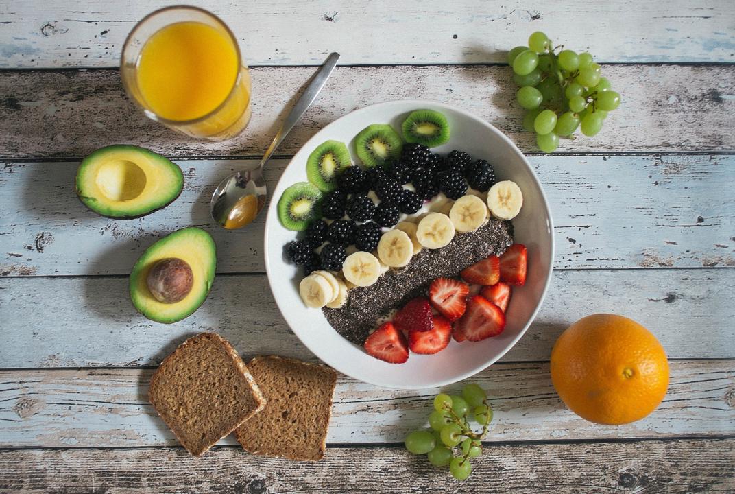 Breakfast table from above with a fruit bowl, avocado, toast and orange juice