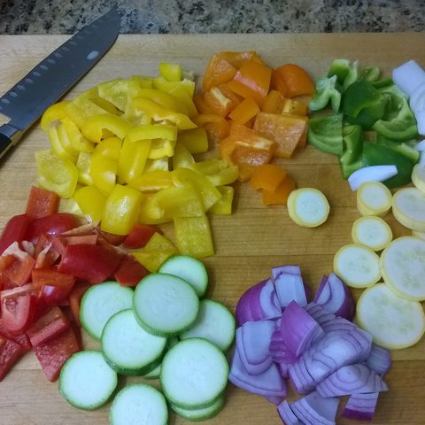 Chopped peppers, zucchini and onion on a wooden board with a knife