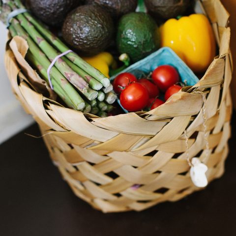 A woven basket of asparagus, tomatoes, avocados and peppers
