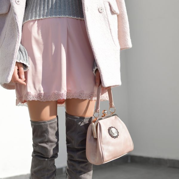 Blush pink handbag with a cameo clasp held beside a pink skirt