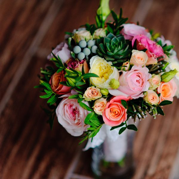 A round posy of pink roses and small succulents on a wooden table