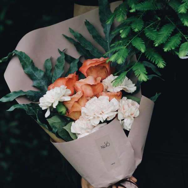 Orange roses and white carnations wrapped in pale paper with ferns