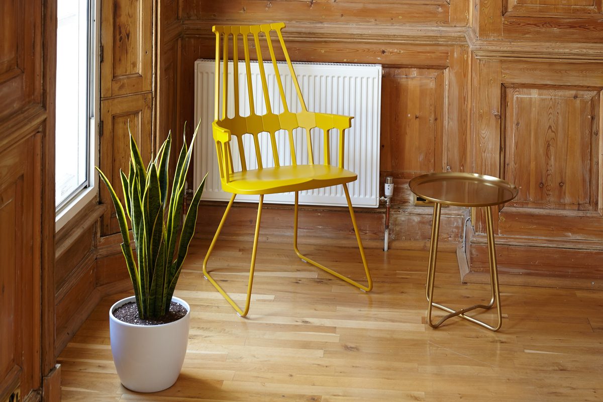 A yellow spindle chair and a potted plant in a sunny wood panelled room