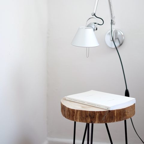 A white swing arm lamp hanging over a small log side table