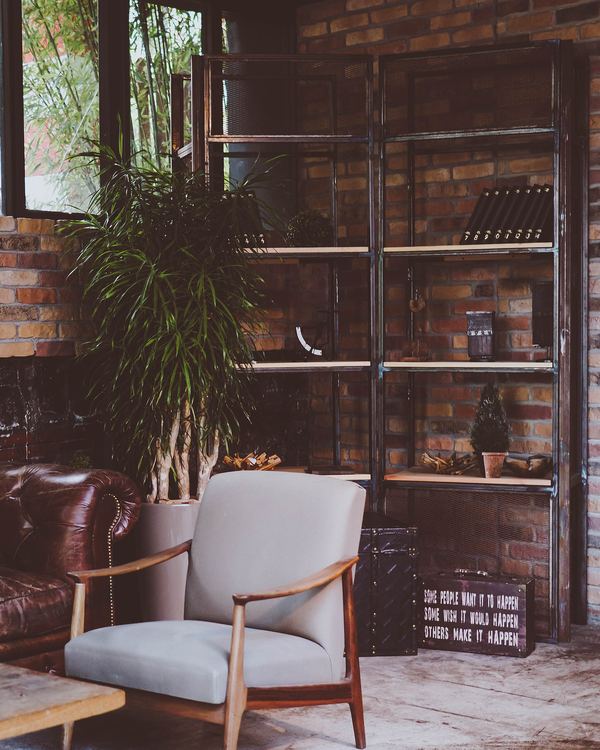 A grey armchair beside a leather sofa in front of a brick wall