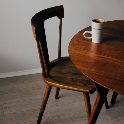 A round walnut table and a dark wooden chair on a pale floor