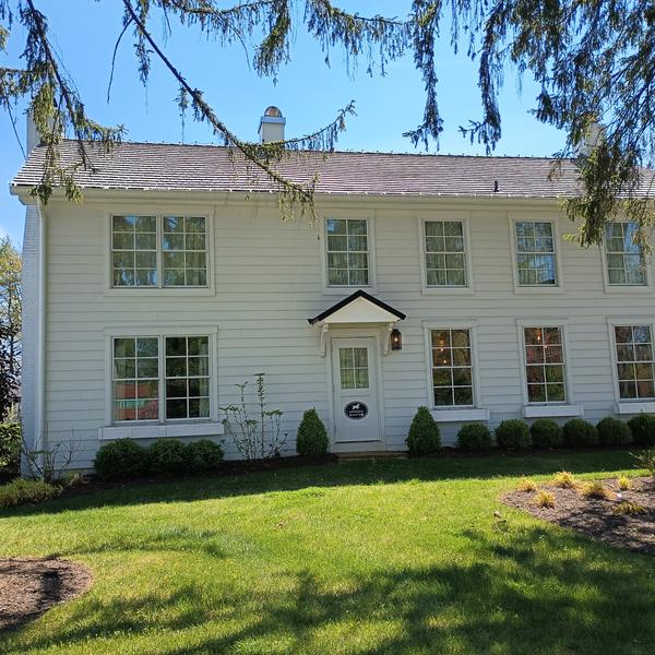A white clapboard colonial house behind a tall evergreen tree