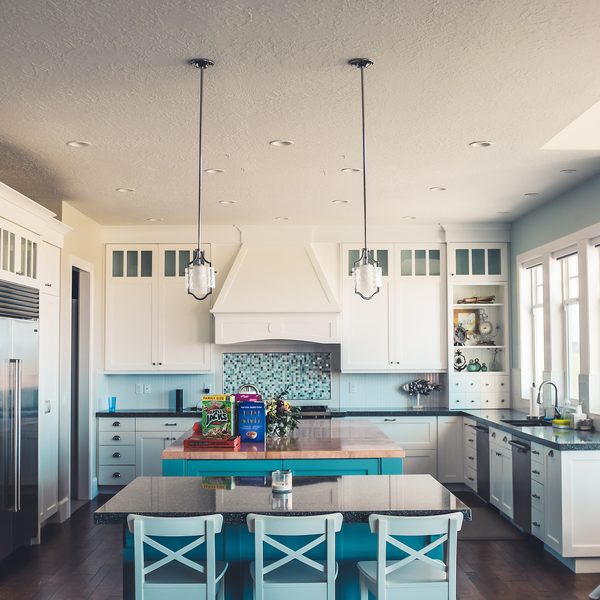 A bright white kitchen with an island, pendant lights and blue tiles