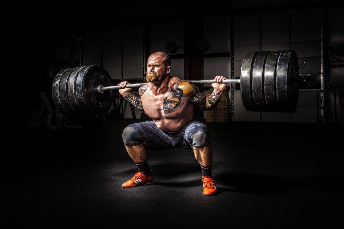 An athlete squatting a loaded barbell under a single light in a dark gym