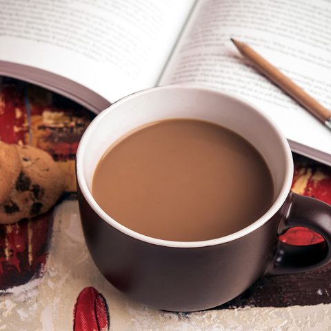 A mug of milky coffee on an open book with a pencil and cookies