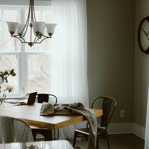 A bright dining room with a wooden table, a chandelier and white curtains